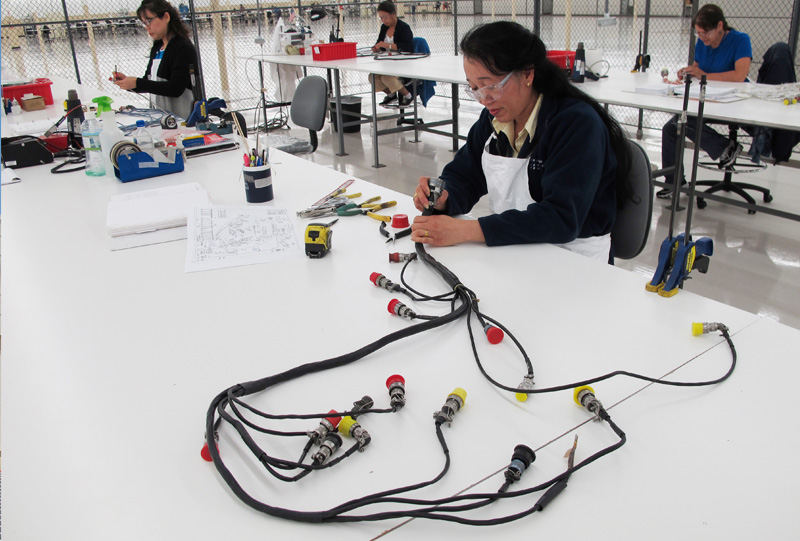 Employee sitting at a bench repairing a connector harness